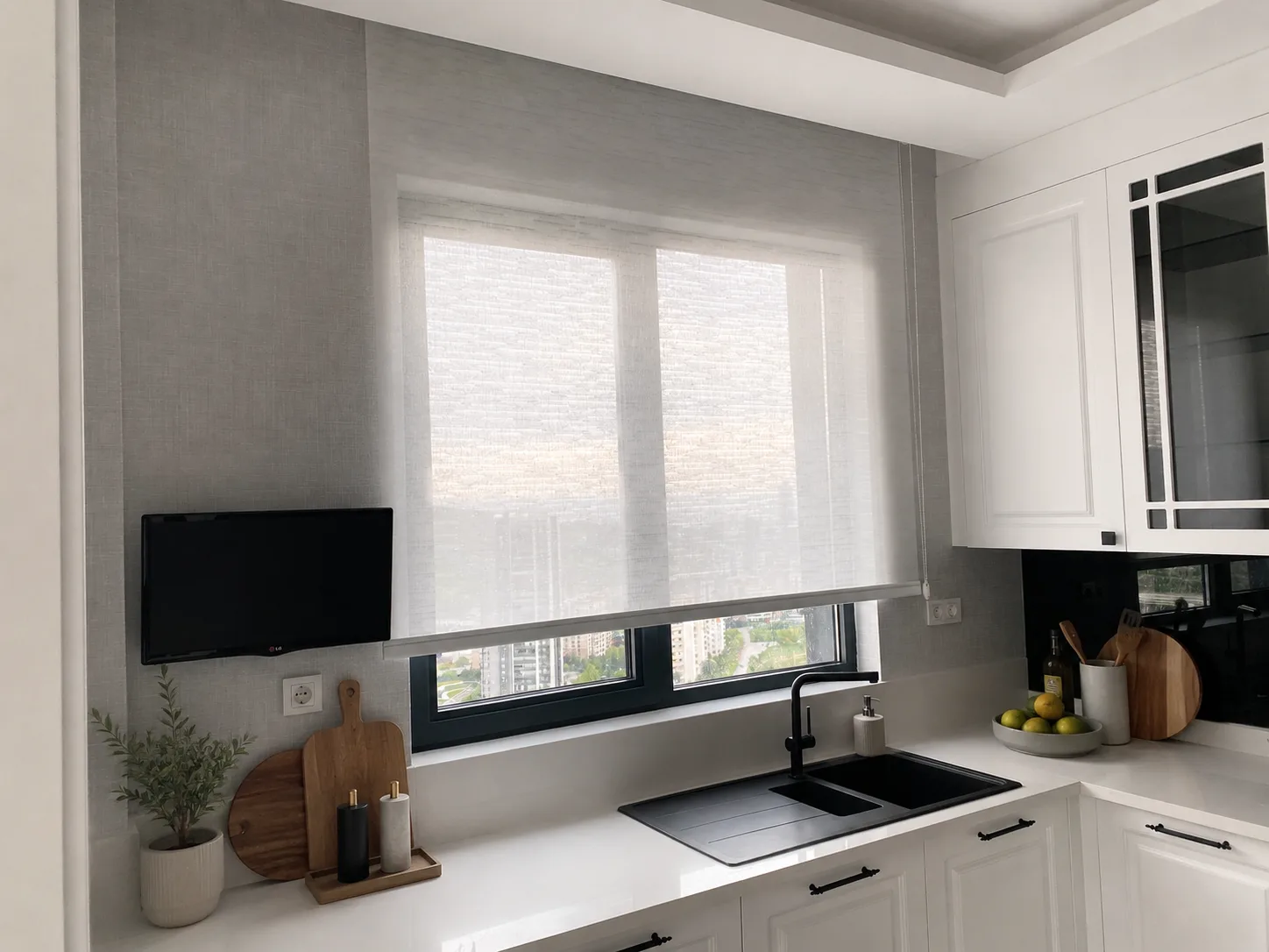 White roller blind on a wide window above the sink in a white kitchen