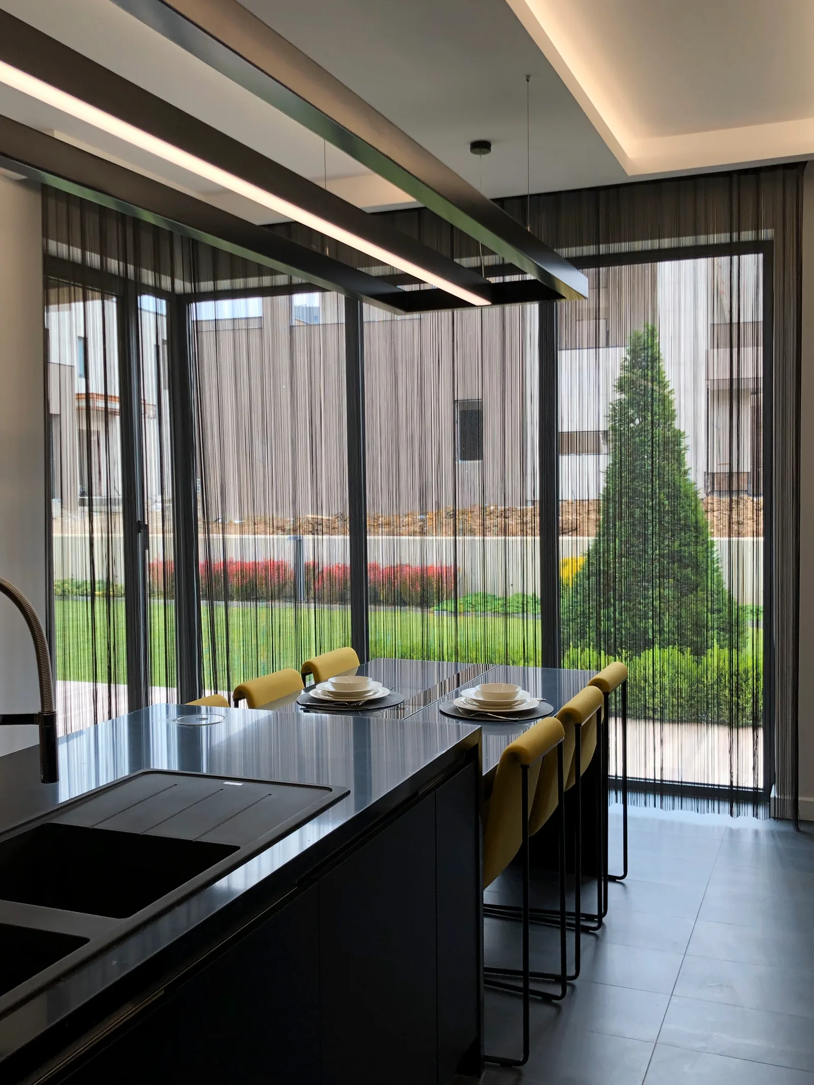 Black string curtains on corner windows beside a kitchen island and dining area