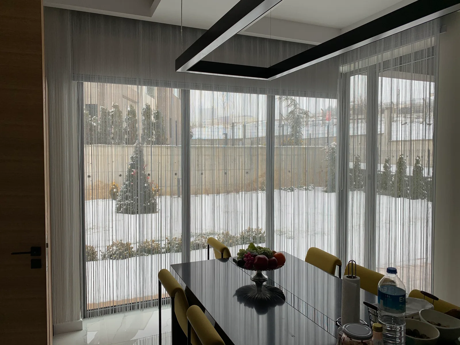 Light-coloured string curtains on corner windows behind a dining table